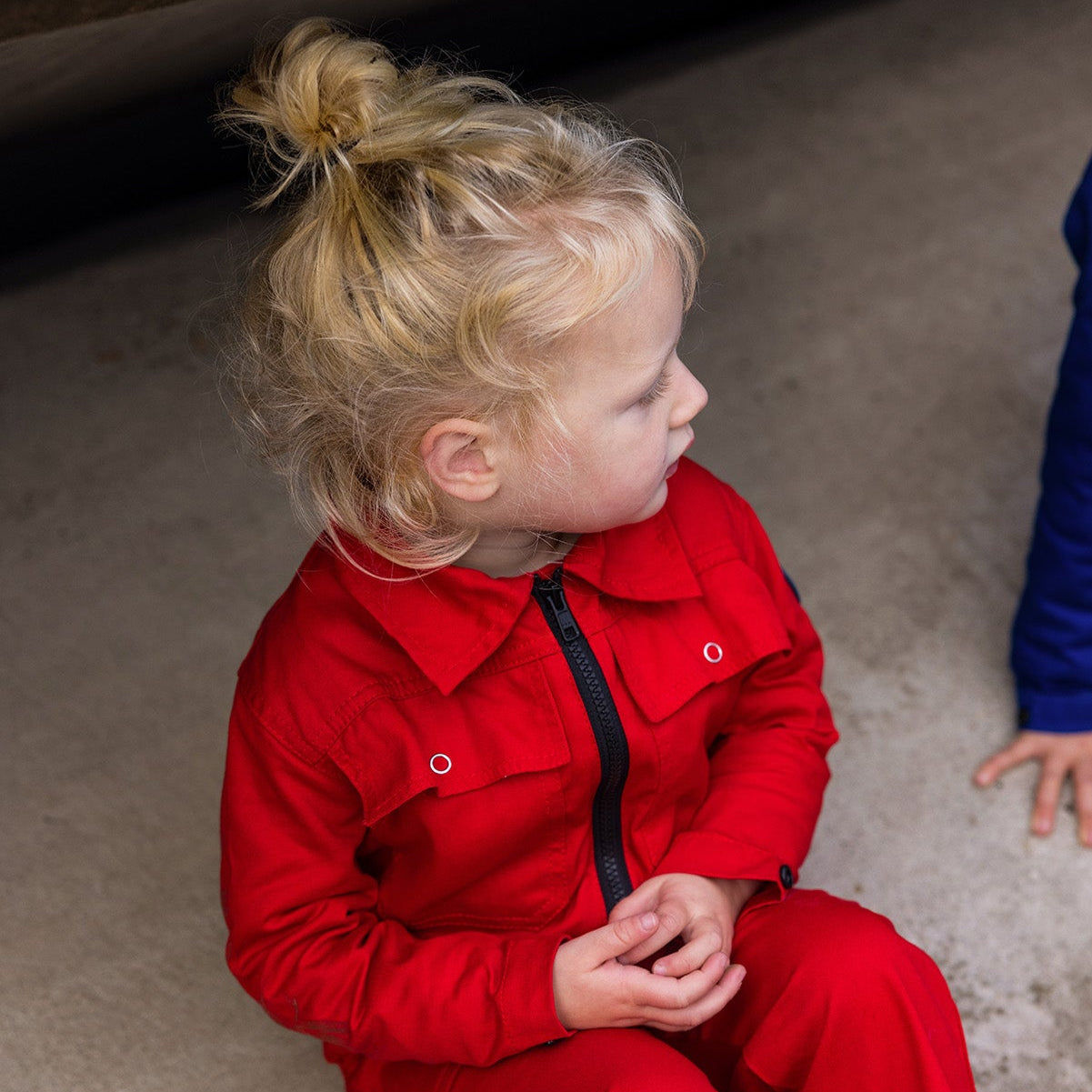 Child wearing a red outfit sitting on the ground